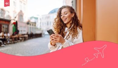 Jeune femme souriante adossée à un mur en vile utilisant son GSM avec une eSIM