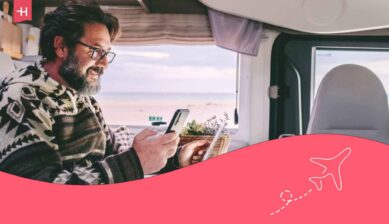 Homme regardant l'écran de son téléphone utilisant ses données mobiles assis face à son ordinateur dans un camping car en voyage