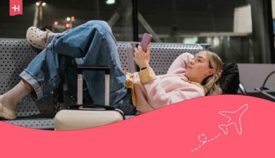Jeune voyageuse reposant sur le banc de l'aéroport avec sa valise et regardant son GSM avec une eSIM Mobile Vikings