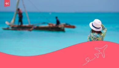 Femme de dos avec un chapeau observant un bateau depuis la plage à Zanzibar