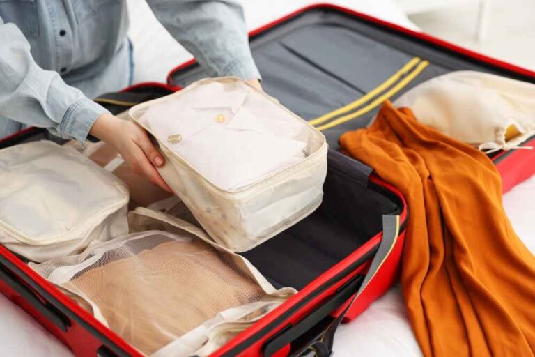 Mains plaçant un cube de rangement rempli dans une valise rouge