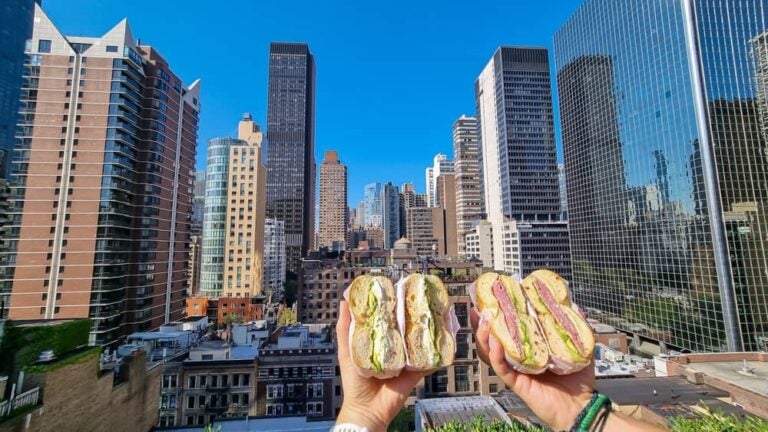 Deux moitiés de bagel garni tenues devant les gratte-ciel, une street food typique de New York