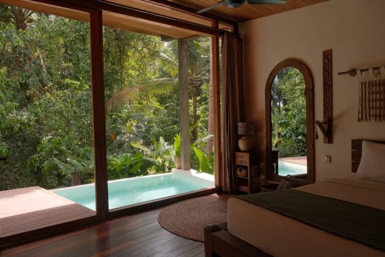 Chambre d'hôtel avec grande baie vitrée ouvrant sur une piscine privée et la végétation tropicale d'Ubud.
