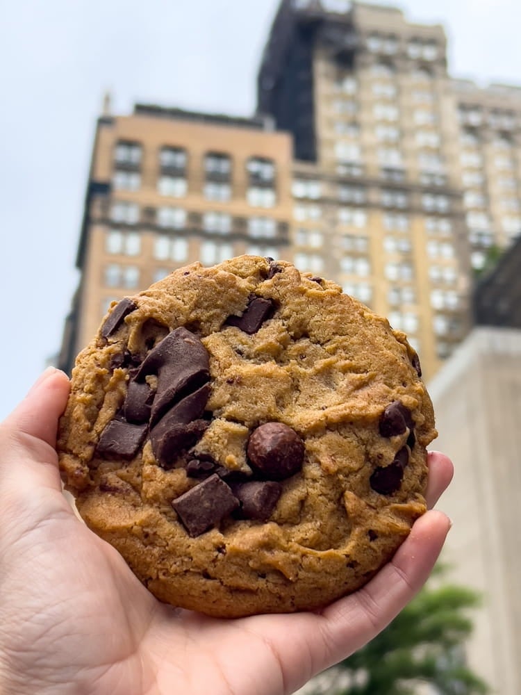 Un immense cookie aux pépites de chocolat tenu à la main dans une rue de Manhattan.