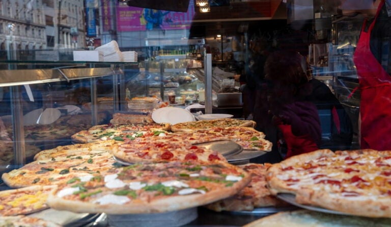 Vitrine de pizzeria exposant de larges pizzas aux garnitures variées, prêtes à être servies à la part.