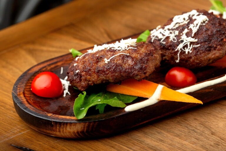 Qofte grillées servies sur une planche en bois, une viande incontournable de la cuisine albanaise.
