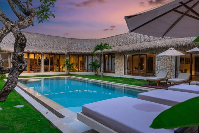 Villa privée avec piscine et toit en chaume traditionnel au crépuscule dans le quartier de Seminyak.