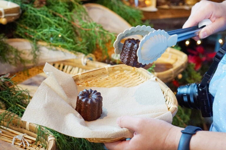 Personne attrapant un cannelé avec une pince sur un étal du marché de Noël.