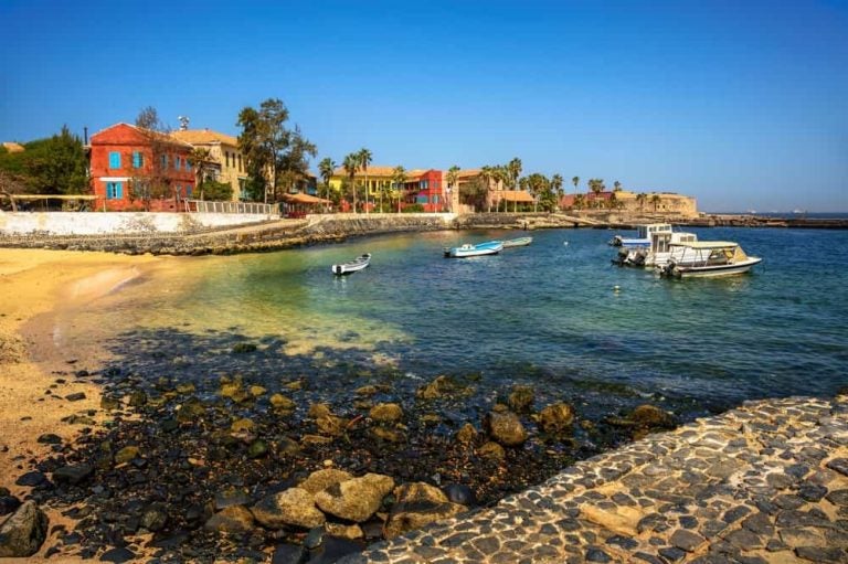 Petits bateaux amarrés devant les bâtiments historiques colorés de l'île de Gorée au Sénégal.