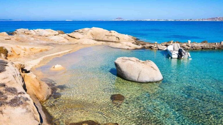 Galets lisses éparpillés sur le rivage sablonneux de la baie d’Orkos, à Naxos, face à une eau turquoise calme et limpide