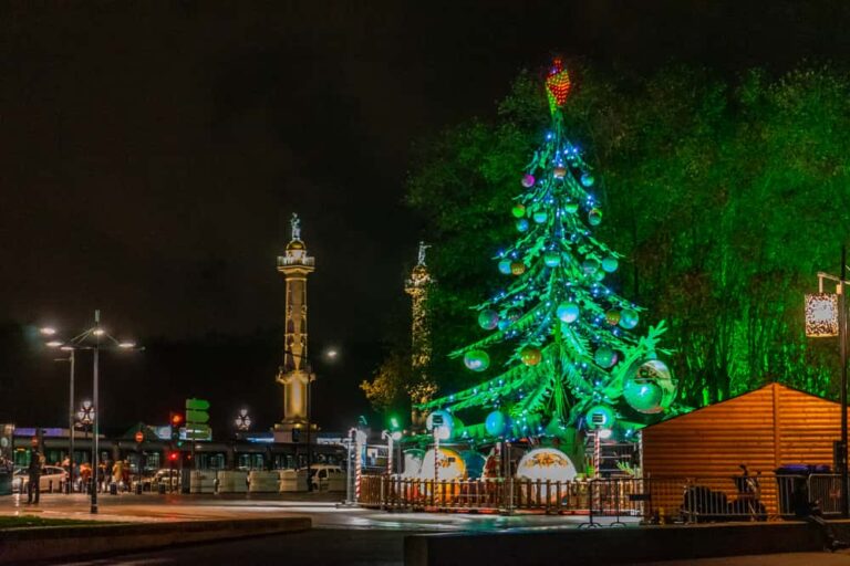 Grand sapin artificiel illuminé en vert la nuit avec les colonnes des Girondins en fond.