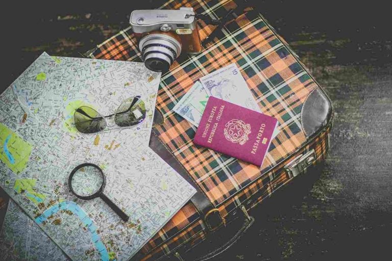 uma maleta com um passaporte, uma câmera, um óculos escuros, uma lupe e mapas