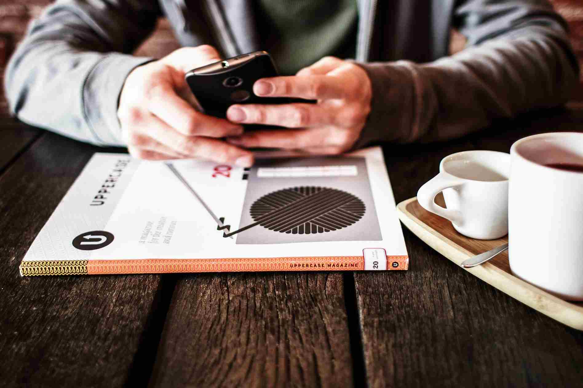 uma homem usando seu celular em uma mesa de uma cafeteria