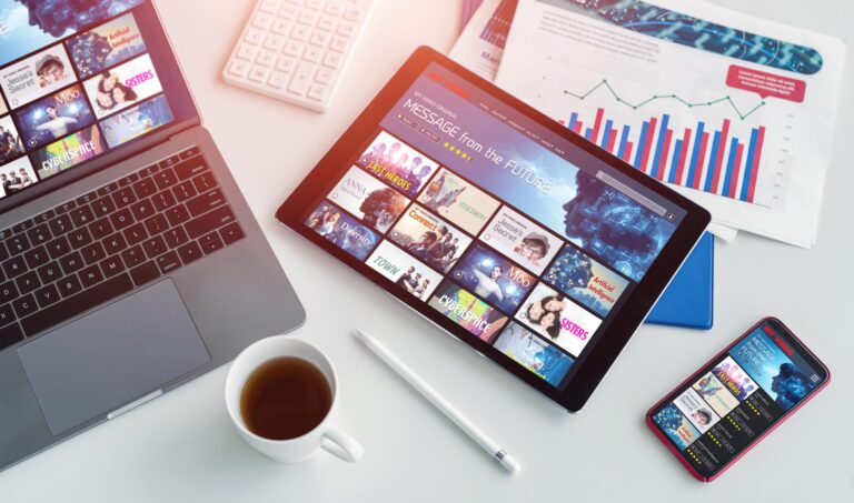m telefone, um tablet, um laptop e uma xícara de café em uma mesa branca.