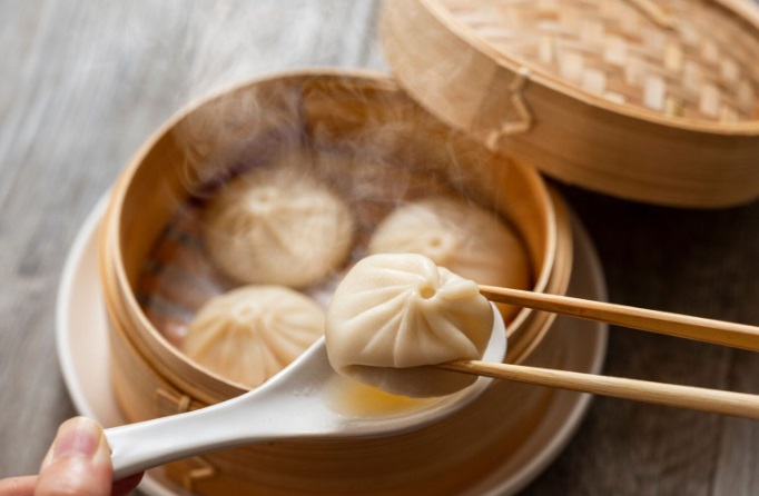 Close de uma pessoa pegando um xiao long bao, ou bolinho de sopa, de uma tigela de bambu cozida no vapor.