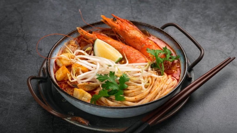 Uma tigela de laksa, com macarrão de arroz grosso e caldo aromático de curry com leite de coco.