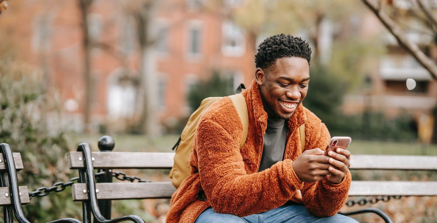 Uomo seduto su una panchina del parco che usa il cellulare