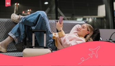 Giovane viaggiatrice che si riposa sulla panchina dell'aeroporto con valigia e smartphone