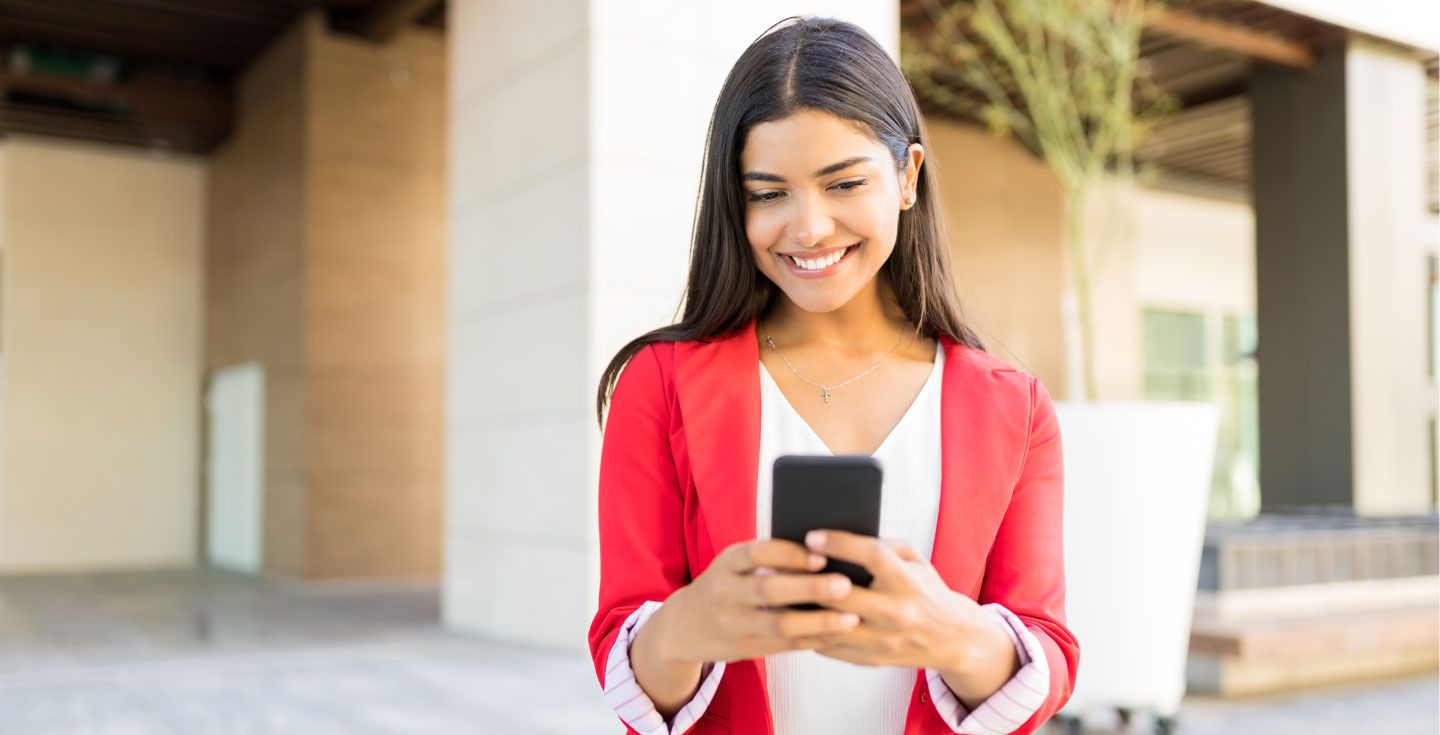 Donna con giacca rossa che guarda il suo cellulare all'aperto