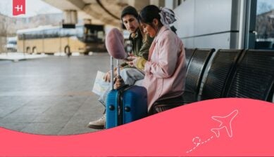 Turisti alla stazione degli autobus accanto alla propria valigia, mentre consultano il telefono