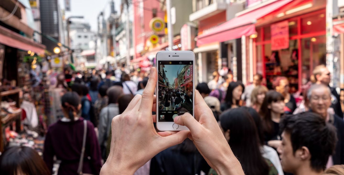 Persona che scatta una foto con il suo telefono in strada in mezzo alla folla.