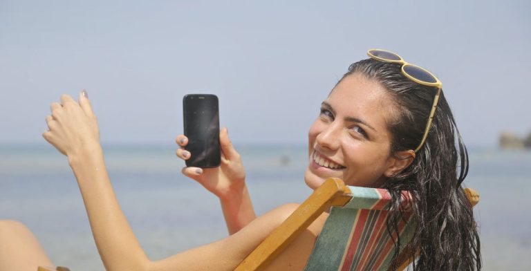 Donna che usa il cellulare seduta sulla spiaggia