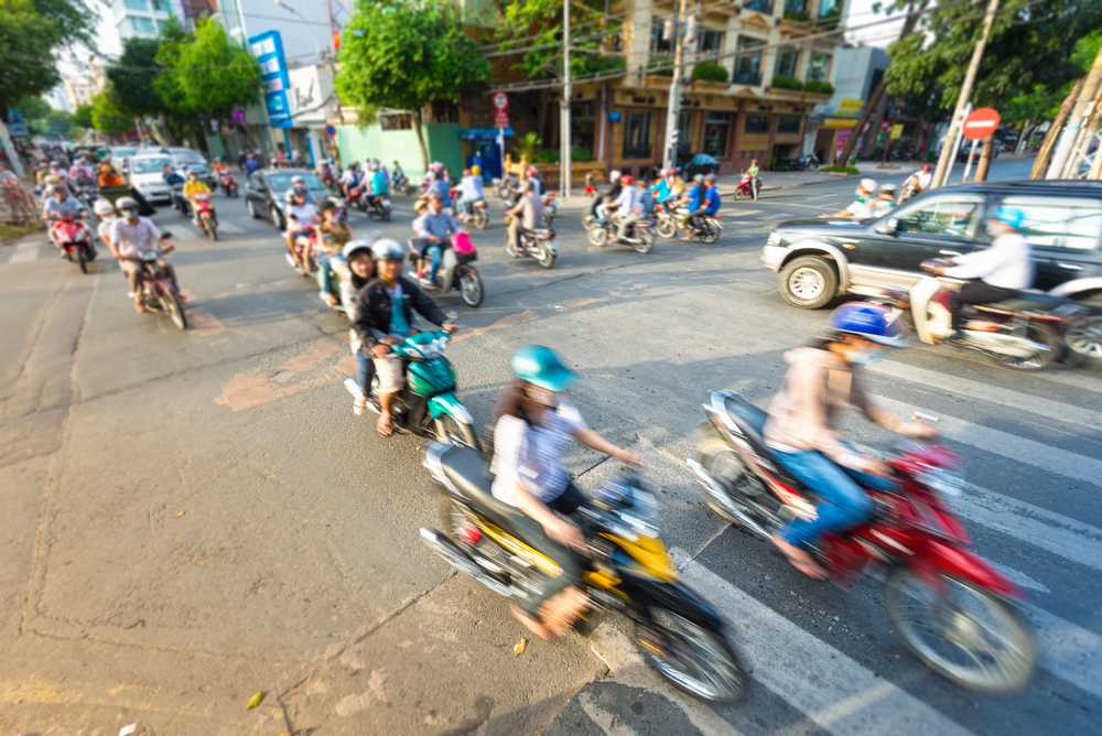 Vista in movimento di una strada in Vietnam. Sud-est asiatico. Traffico quotidiano intenso con flusso di moto e auto. Vista sfocata di biciclette in primo piano. Trasporti e traffico.
