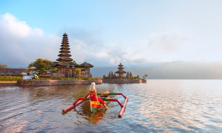 Giovane ragazza bionda in abito rosso tradizionale nella barca vicino al tempio Pura Ulun Danu Bratan - tempio indù sul lago Bratan - isola di Bali, Indonesia