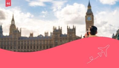 Giovane turista con occhiali da sole e abbigliamento casual che tiene in mano uno smartphone mentre è in piedi davanti al Big Ben e alla barriera della torre dell'orologio a Londra.