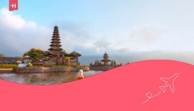 Giovane ragazza bionda in abito rosso tradizionale nella barca vicino al tempio Pura Ulun Danu Bratan - tempio indù sul lago Bratan - isola di Bali, Indonesia