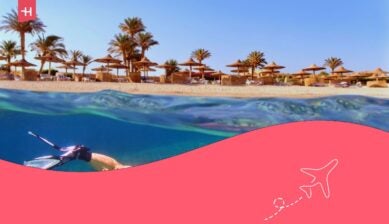 Una donna che fa snorkeling nei pressi della barriera corallina tropicale. Spiaggia con palme e ombrelloni sullo sfondo, Mar Rosso, Egitto