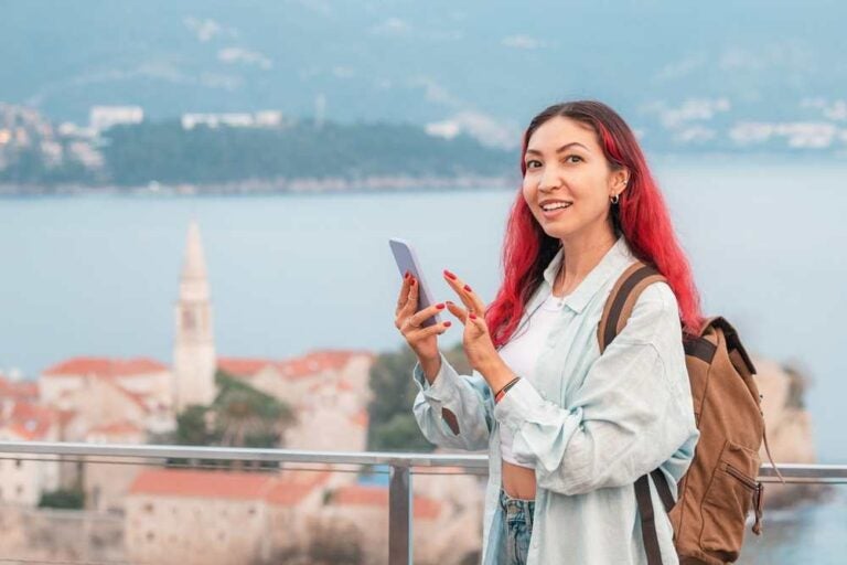 Una turista con uno zaino e un cellulare in mano, sullo sfondo di Budva, in Montenegro, 