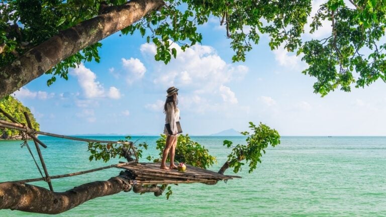 Donna in piedi su un ramo di un albero, spiaggia di Krabi, Thailandia.