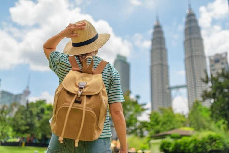 Turista femminile in cappello con zaino godendo di meraviglioso paesaggio urbano a Kuala Lumpur, Malesia.