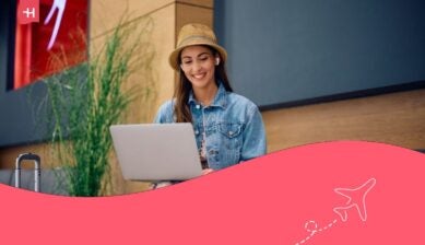 Giovane donna sorridente che usa il computer mentre attende il suo volo nell'area partenze.