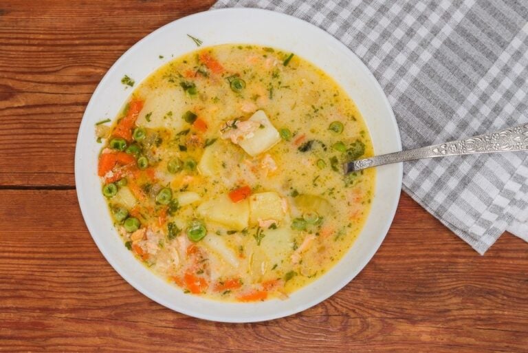 Porzione di zuppa cremosa calda con salmone, scampi, cozze e verdure in ciotola bianca con cucchiaio.