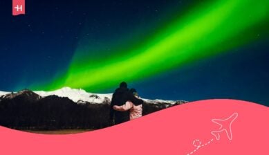Una coppia si abbraccia in una fredda notte, in piedi ad ammirare l’aurora boreale sulle cime innevate dell’Islanda.