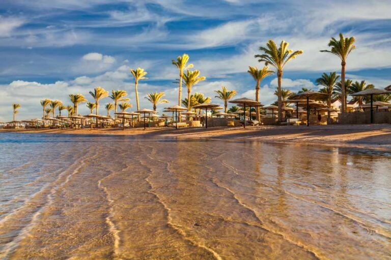 Tramonto sulla spiaggia di Hurghada con palme, ombrelloni e lettini.