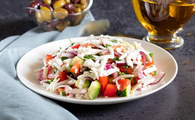 Insalata Shopska con verdure e brynza su sfondo scuro con tessuti grigi.