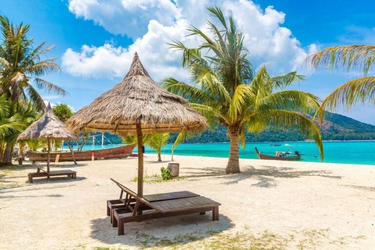 Ombrellone, lettino e palma su una spiaggia tropicale in una giornata di sole.