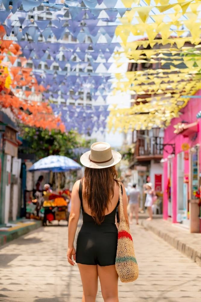 Un'elegante donna latina, vestita di nero e con un cappello di paglia, passeggia nel vivace quartiere di Getsemaní a Cartagena