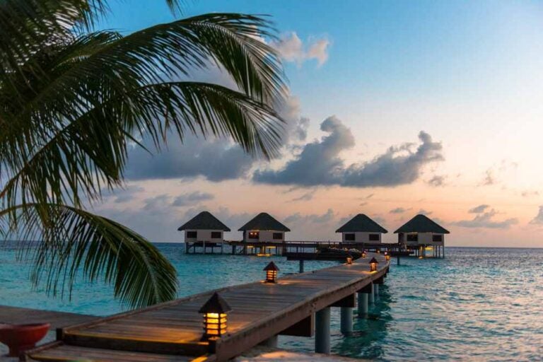 Foto grandangolare del sentiero di legno che conduce alle camere affacciate sulle acque turchesi di un’isola vicino a Maafushi, alle Maldive, al tramonto.