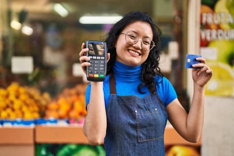 Giovane dipendente cinese con in mano un cellulare e una carta di credito in un negozio di frutta.