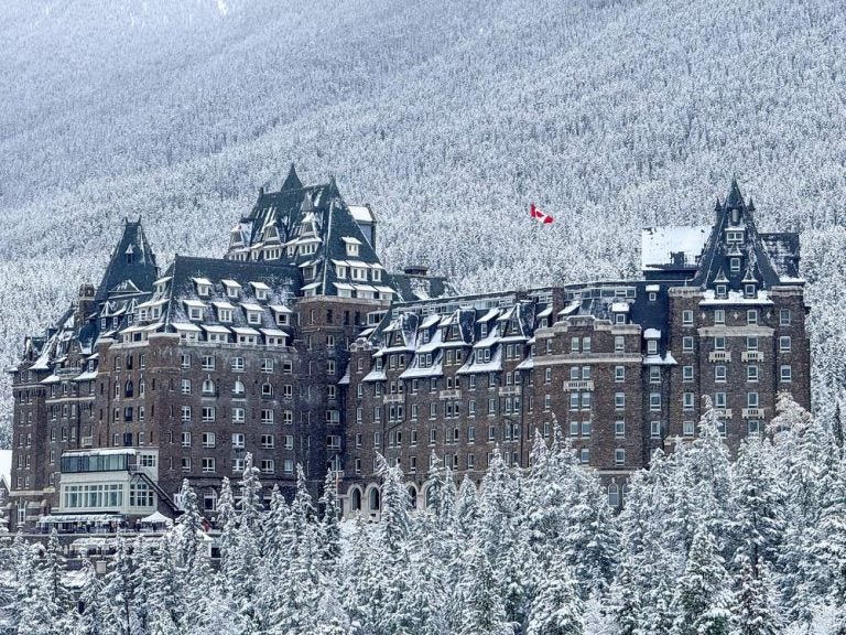 Dettagliato scatto esterno dello storico Stone Castle Hotel con i suoi caratteristici tetti verdi ricoperti di neve fresca, immersi in una fitta foresta di pini innevati.