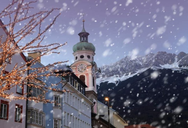 I tetti di Innsbruck con le montagne sullo sfondo e le luci natalizie in primo piano in una serata invernale.