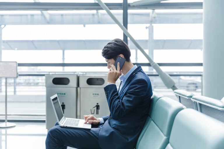 공항에서 스마트폰과 노트북을 사용하며 통화하는 비즈니스맨