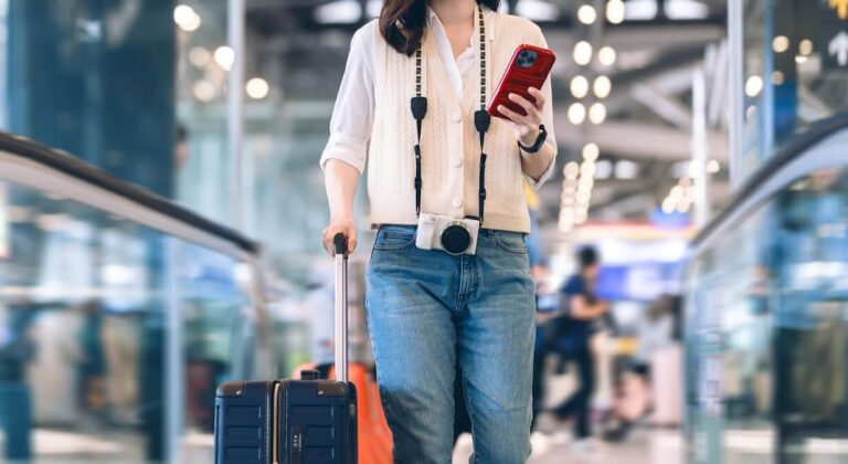 공항에서 여행 가방을 끌고 스마트폰을 사용하는 여성 여행객