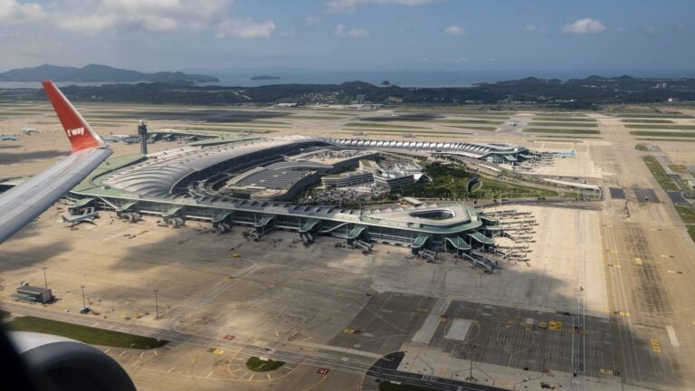 Aerial view of a large airport terminal building and runways, seen from an airplane wing during takeoff or landing.