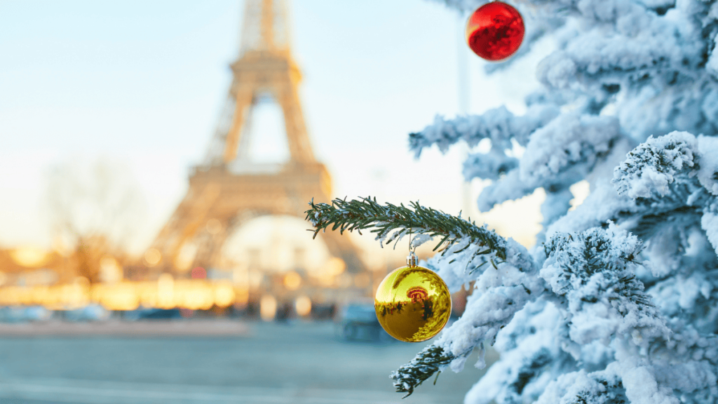 Foto van een besneeuwde kerstboom met twee kerstballen en de Eiffeltoren op de achtergrond