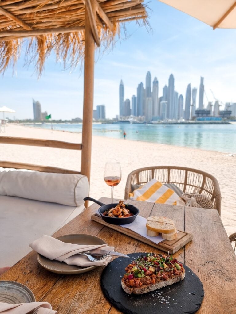 Foto van een restaurant op het strand met de skyline van Dubai op de achtergrond